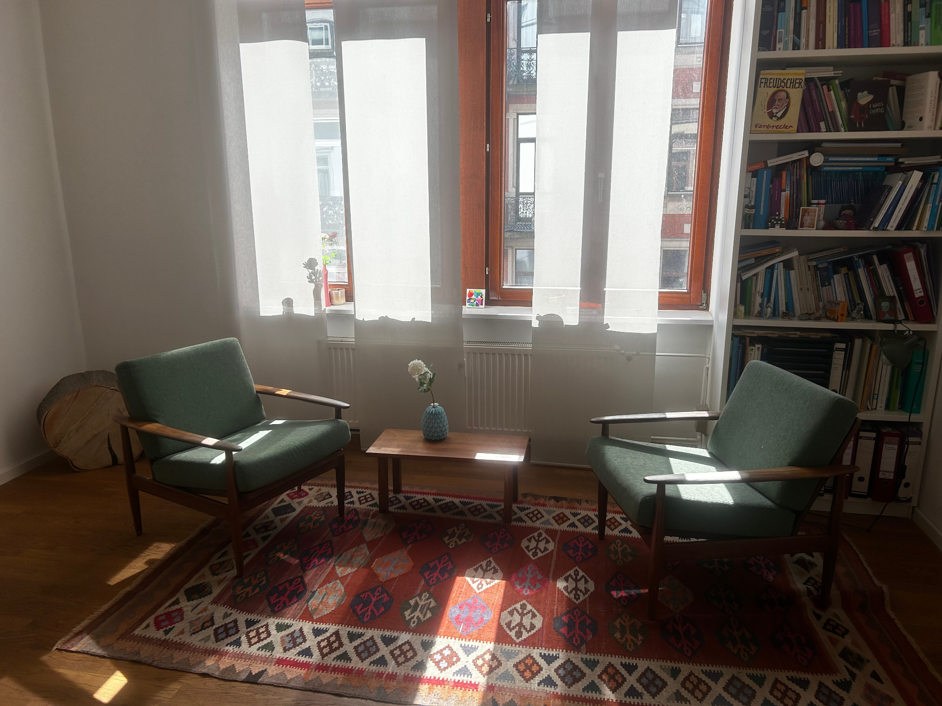 Therapieraum der Praxis: zwei grüne Sessel, Bücherregal und warmes Tageslicht